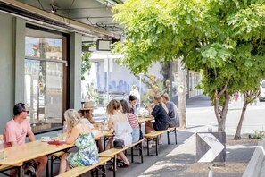 An outdoor café with tables and chairs, a tree, and a cityscape view. - Light and Cosy Footscray Studio | Inner-West Stay (Footscray)