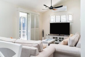 Una sala de estar con un sofá, un televisor de pantalla plana, un ventilador de techo y un ventanal corredero.