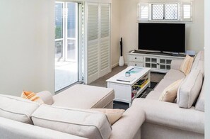 A living room with a sofa, coffee table, TV, and a sliding door leading to an outdoor area. - Coastal Calm on the Fraser Coastl (Poona)