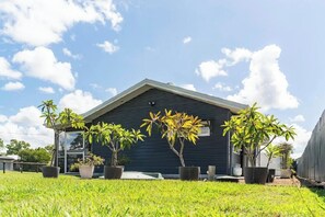 A modern building with a dark exterior, surrounded by well-maintained grass and several potted plants. - Coastal Calm on the Fraser Coastl (Poona)