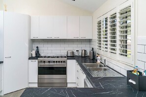 A modern kitchen with white cabinets, a gas stove, a sink, and a window with blinds. - Coastal Calm on the Fraser Coastl (Poona)
