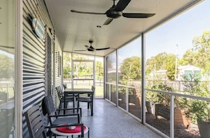 A covered porch with a table and chairs, a ceiling fan, and large windows offering a view of the outdoors.