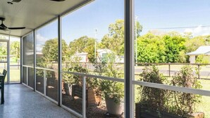 Un espace extérieur abrité, doté de grandes fenêtres, de ventilateurs de plafond et de plantes en pot.