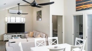 Un salon moderne comprenant un canapé, un téléviseur, un ventilateur de plafond et un coin repas avec des chaises.