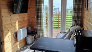 L’intérieur d’un chalet en bois comprend une table à manger, des chaises, un téléviseur fixé au mur, un radiateur et une vue sur l’extérieur grâce à une porte vitrée.
