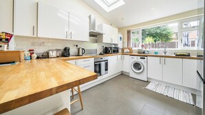 A modern kitchen with white cabinets, a wooden countertop, a skylight, a washing machine, and a window with a view of the outside. - House Sleeps 4 - Free Parking and Garden (Manchester)