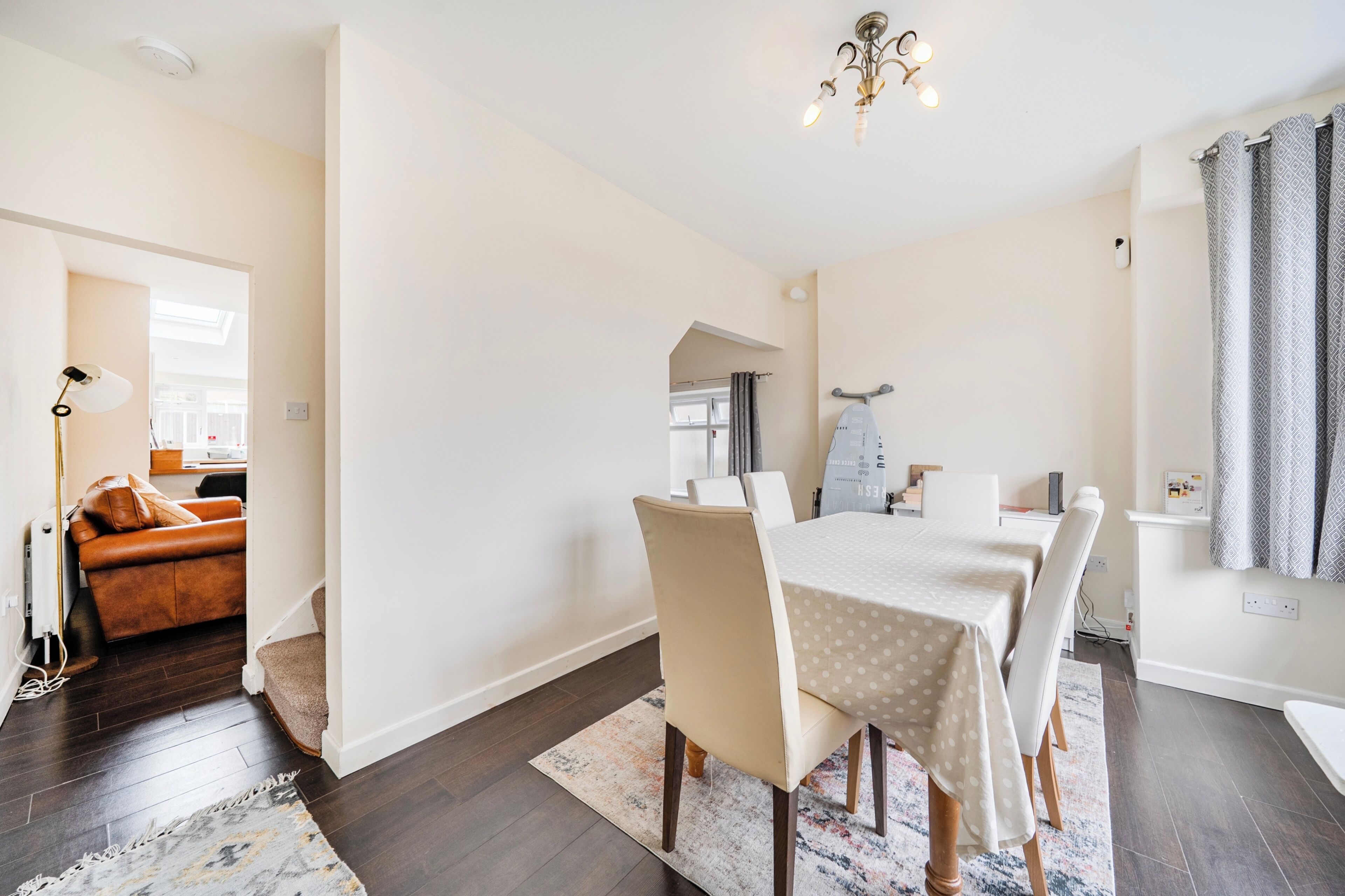 Een eetruimte met een tafel voor vier personen, een bank op de achtergrond en een kroonluchter erboven.
