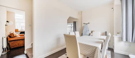 Een eetruimte met een tafel voor vier personen, een bank op de achtergrond en een kroonluchter erboven.
