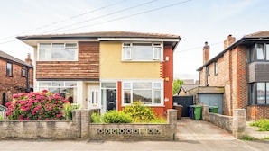 A two-story residential building with a brick facade, a front garden with flowering plants, and a visible garage door. - House Sleeps 4 - Free Parking and Garden (Manchester)