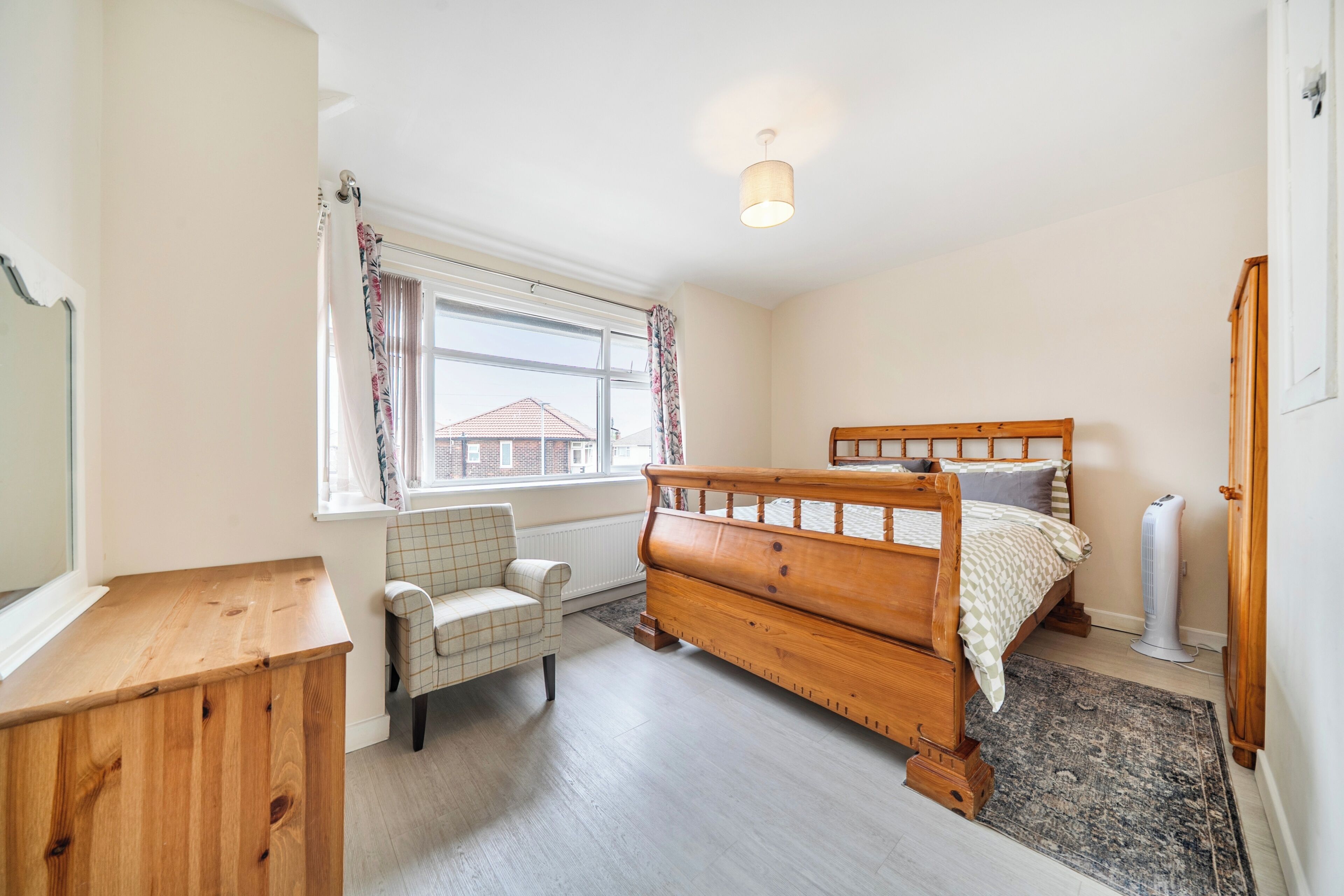 Une chambre à coucher avec un lit en bois, une chaise, un radiateur, une fenêtre avec des rideaux et un radiateur portatif.