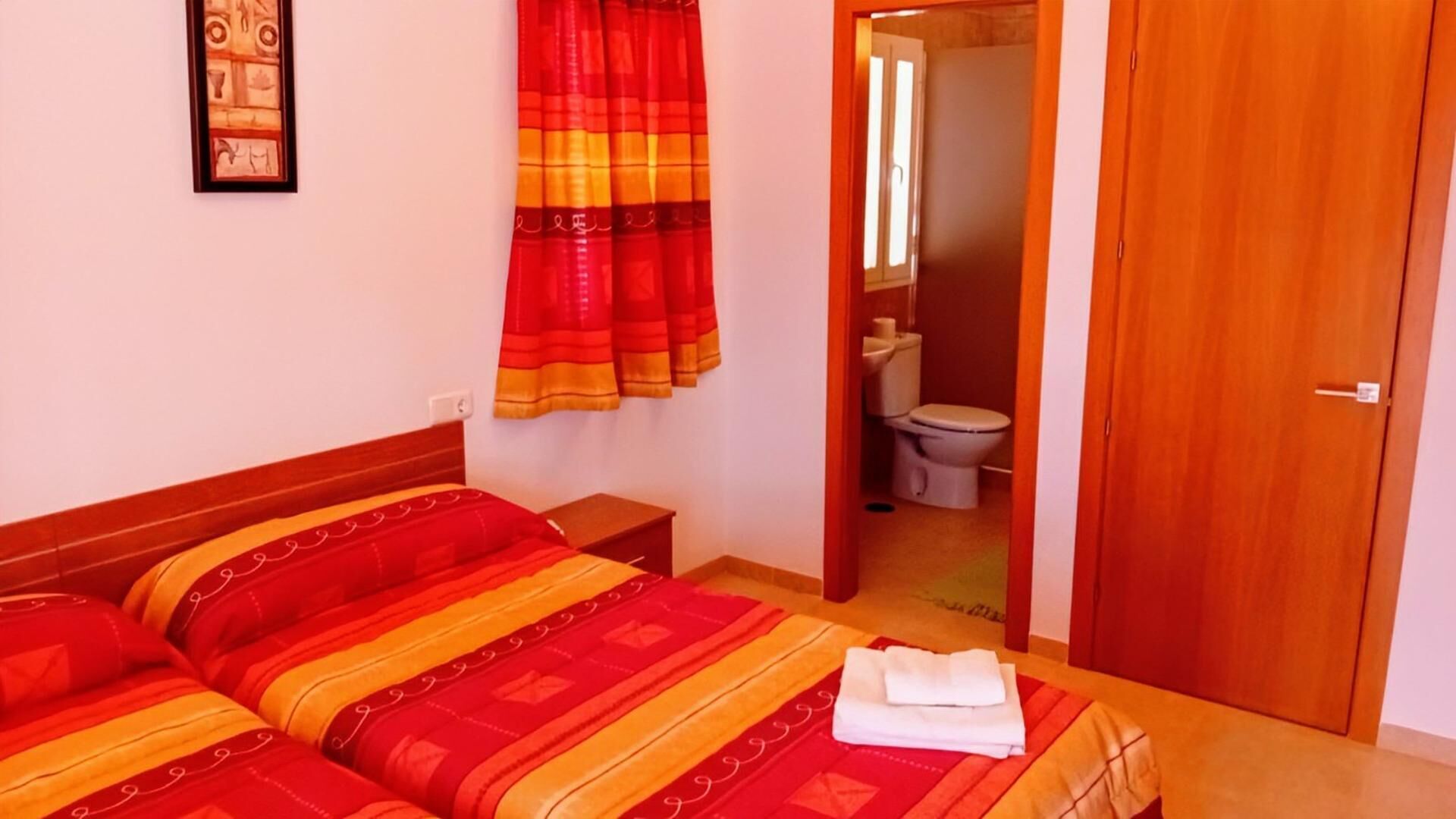 A hotel room with two beds, a wooden headboard, a bathroom visible through an open door, and a framed picture on the wall.