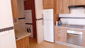 A compact kitchen with wooden cabinets, a white refrigerator, a washing machine, and a stove. - Beautiful House, Sleeps 7 With Private Pool (Iznajar)