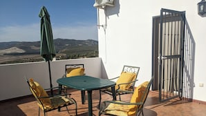 A terrace with a table and chairs, a green umbrella, and a view of hills. - Beautiful House, Sleeps 7 With Private Pool (Iznajar)