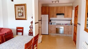 A compact kitchen with wooden cabinets, a refrigerator, a stove, and a dining area with a table and chairs. - Beautiful House, Sleeps 7 With Private Pool (Iznajar)