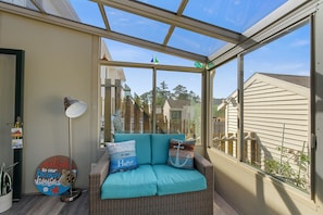 A sunroom with a wicker sofa, a lamp, and a welcome sign. - Sunrise/Sunset | Affordable townhome close to Park & Carnival! (Chincoteague Island)