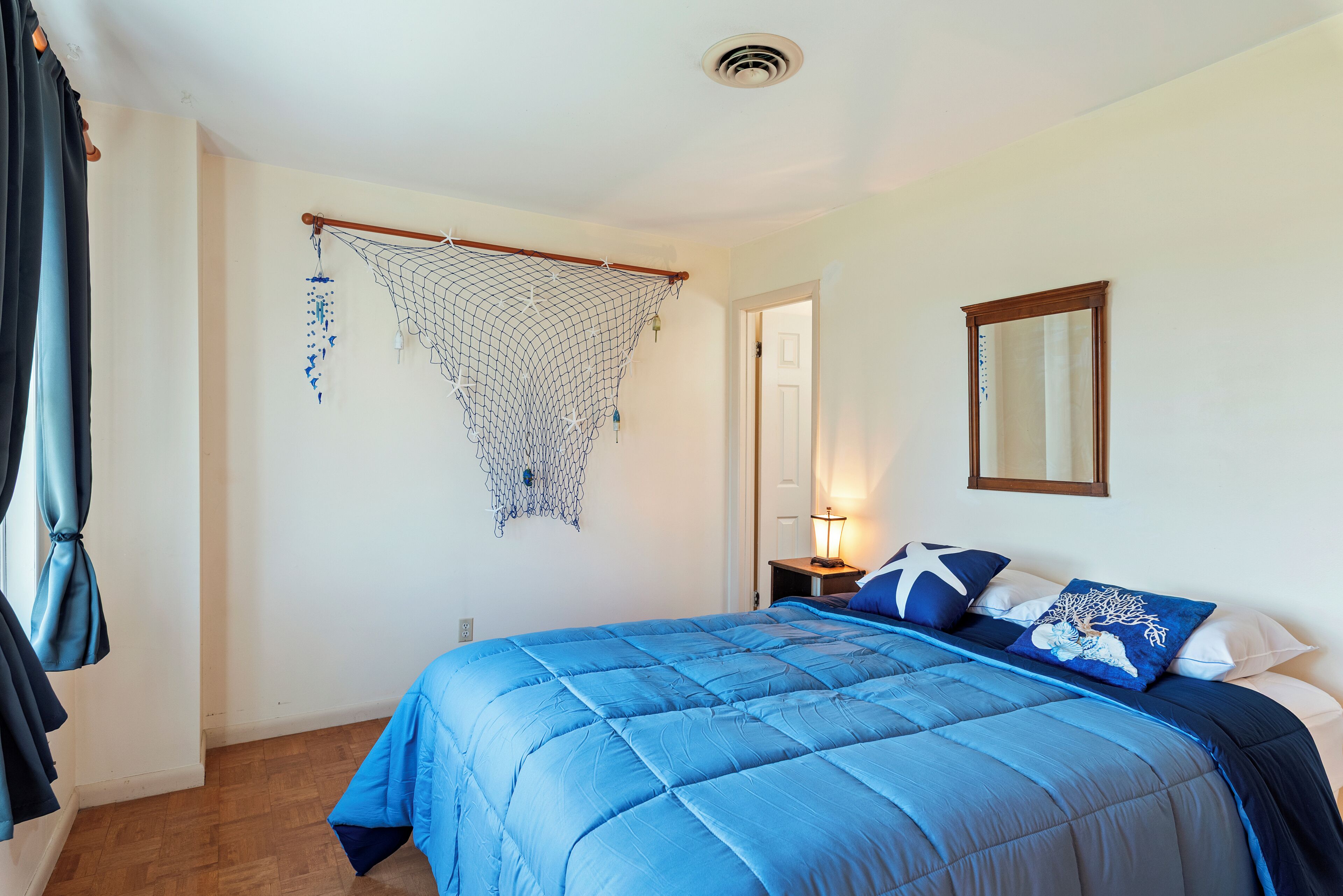 Une chambre avec une couvre-lit bleue, une décoration en forme de moustiquaire suspendue, une lampe de chevet et un miroir au mur.