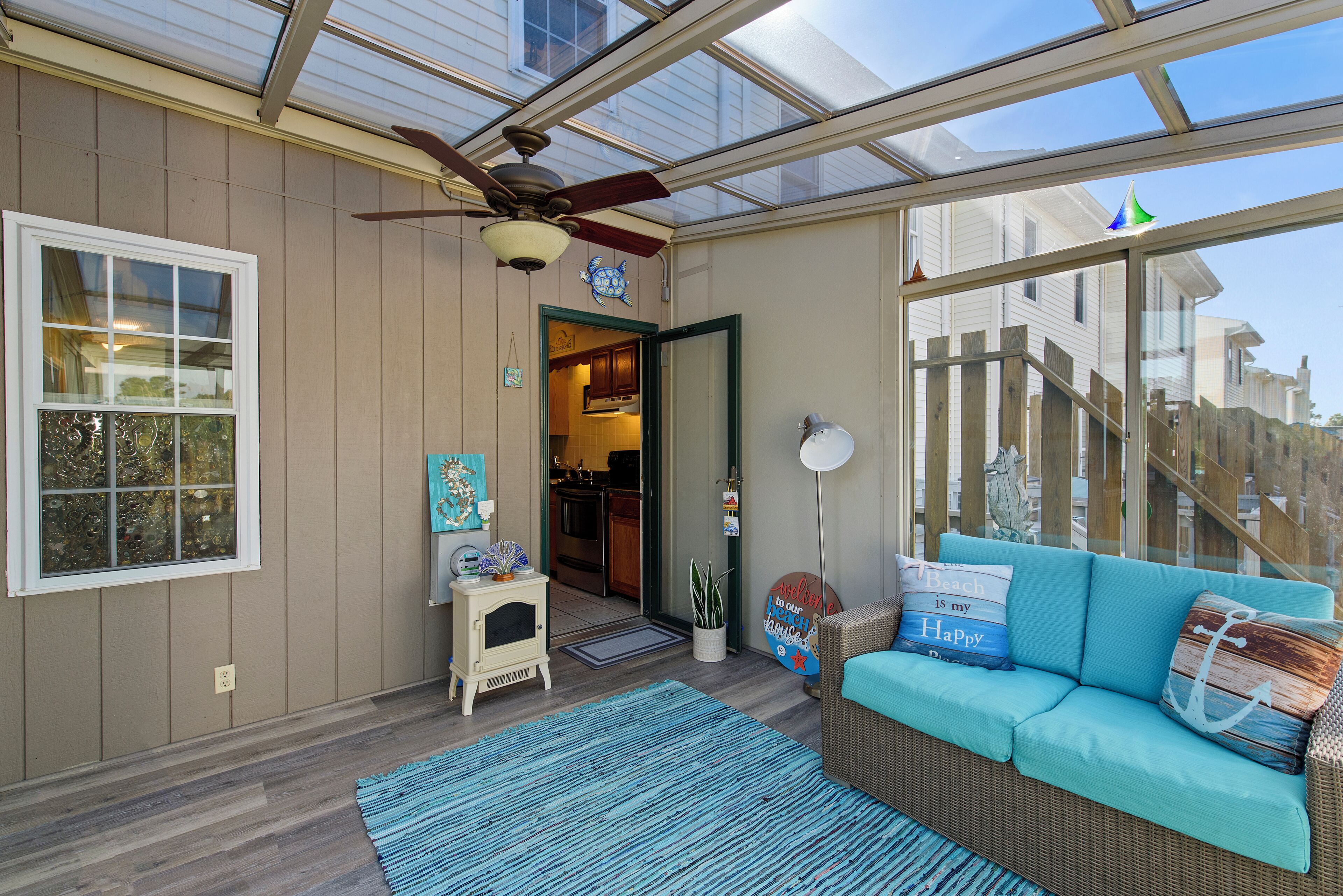 A sunroom with a ceiling fan, a sofa with cushions, a small table with decorative items, and a view of the outside.