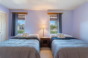 Ein Schlafzimmer mit zwei Betten, einem Nachttisch, einer Lampe und einem Fenster mit Vorhängen.
