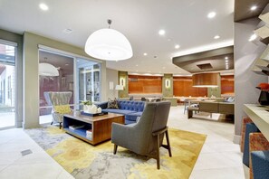 Eine moderne Hotellobby mit Sitzgelegenheit, einer Rezeption und Blick auf die Stadt.
