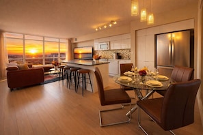 A modern kitchen with a large refrigerator, a dining area with a glass table, and a sofa set.