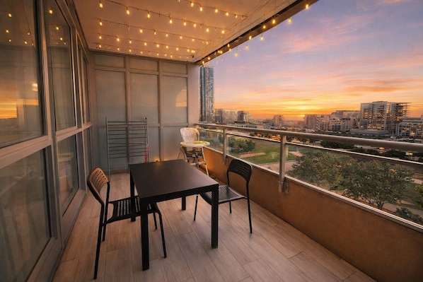 A balcony with a table and chairs, overlooking a cityscape at sunset. - Bright 2BR Condo Near Rogers Centre, CN Tower & Waterfront (Toronto)
