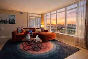Ein modernes Wohnzimmer mit einem Ecksofa, einem Couchtisch und Blick auf einen Sonnenuntergang durch große Fenster.