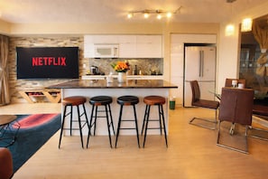 Eine moderne Küche mit einer zentralen Kochinsel, Barhocker, einer Mikrowelle und einem Fernseher, der 'NETFLIX' anzeigt.