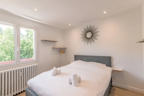 Ein ordentlich bezogenes Bett mit Handtüchern, einem Heizkörper, einem Wandspiegel und einem Regal mit einer kleinen Pflanze.