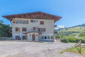 Ein mehrstöckiges Gebäude mit einem geneigten Dach, einer Schotterauffahrt und einer Berglandschaft im Hintergrund.