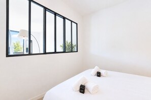 Une chambre d’hôtel avec une grande fenêtre, un lit avec deux serviettes roulées et un panneau de bienvenue posé sur le lit.