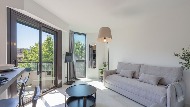 A modern living room with a sofa, a round table, and a dining area with chairs. - Le Cosy Azuréen - Welkeys (Antibes)