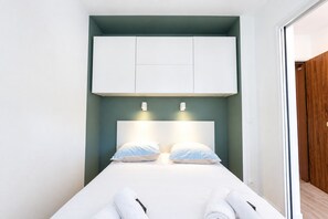 A single bed with white linens and two pillows, a white headboard, and a white cabinet above. - Le Cosy Azuréen - Welkeys (Antibes)