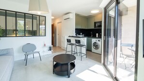 A modern kitchen with a washing machine, a dining area with a table and chairs, and a large sliding glass door leading to an outdoor area. - Le Cosy Azuréen - Welkeys (Antibes)