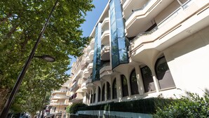 A multi-story building with balconies, a gated entrance, and a street with parked cars. - Le Cosy Azuréen - Welkeys (Antibes)