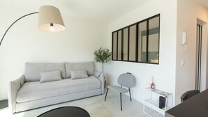 A modern living room with a sofa, a chair, a small table, a lamp, and a framed picture on the wall. - Le Cosy Azuréen - Welkeys (Antibes)