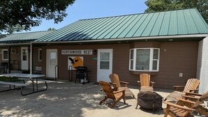 A building with a green roof, a sign reading 'Northwood Nest,' outdoor seating with wooden chairs, and a picnic table. - Family-friendly log cabin style house by Lewis & Clark Lake at DJ's Resort (Yankton)