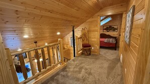 A wooden cabin with a loft bedroom, a staircase, and a view of the outside. - Family-friendly log cabin style house by Lewis & Clark Lake at DJ's Resort (Yankton)
