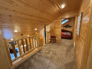 A wooden cabin with a loft bedroom, a staircase, and a view of the outside.