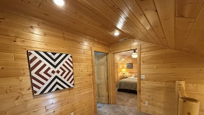 A wooden interior with a hallway leading to a bedroom, a chevron-patterned wall art, and a ceiling light. - Family-friendly log cabin style house by Lewis & Clark Lake at DJ's Resort (Yankton)