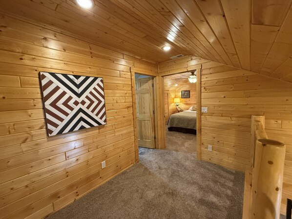 A wooden interior with a hallway leading to a bedroom, a chevron-patterned wall art, and a ceiling light.
