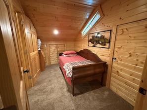 A wooden cabin bedroom with a bed, a nightstand, a dresser, and a window.