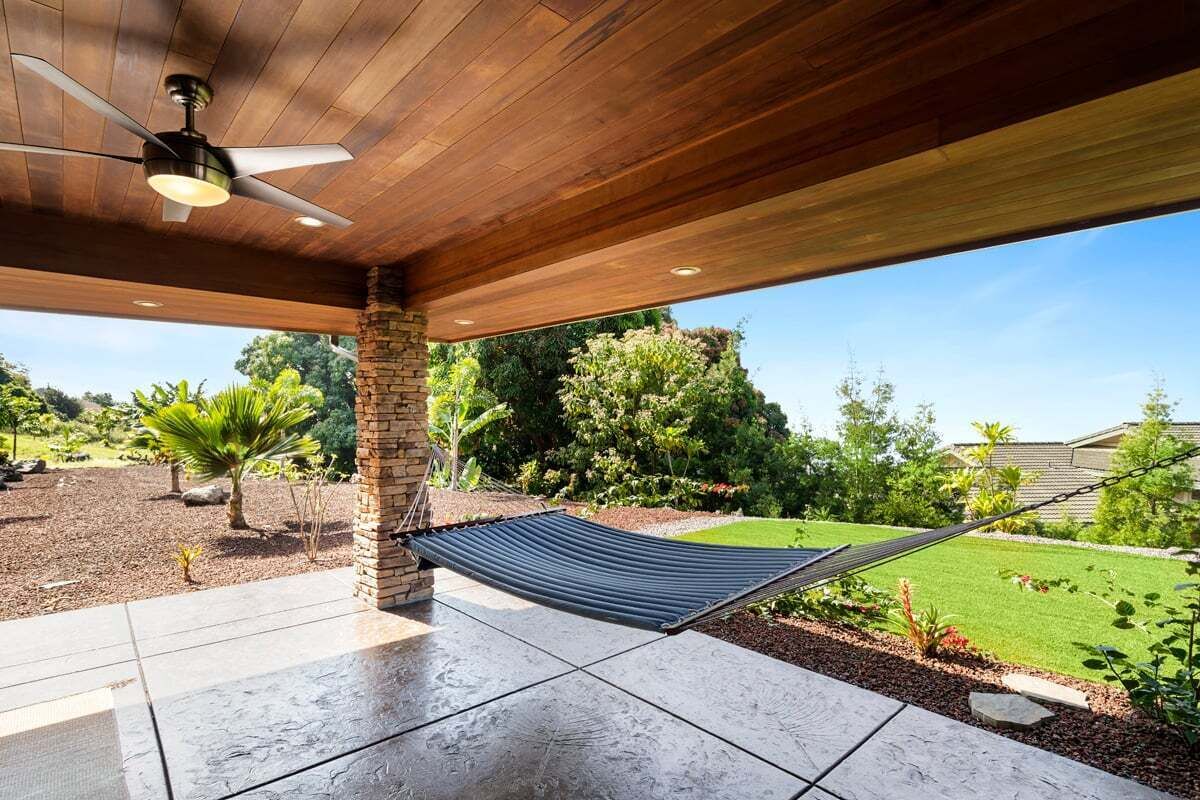 Ein überdachter Patio-Bereich mit Hängematte, Deckenventilator und Blick auf einen gepflegten Garten.