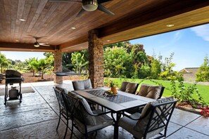 Eine Terrasse im Freien mit Tisch und Stühlen, einem Deckenventilator und Blick auf einen angelegten Garten.