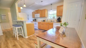 Una cocina con armarios de madera, una encimera blanca, una mesa de comedor de madera y un taburete.