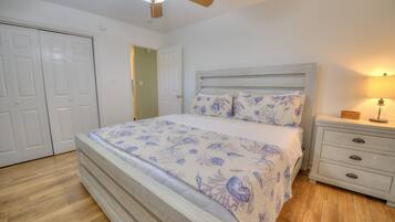 Une chambre à coucher comprenant un lit, une table de chevet, une lampe, un ventilateur de plafond et une porte.