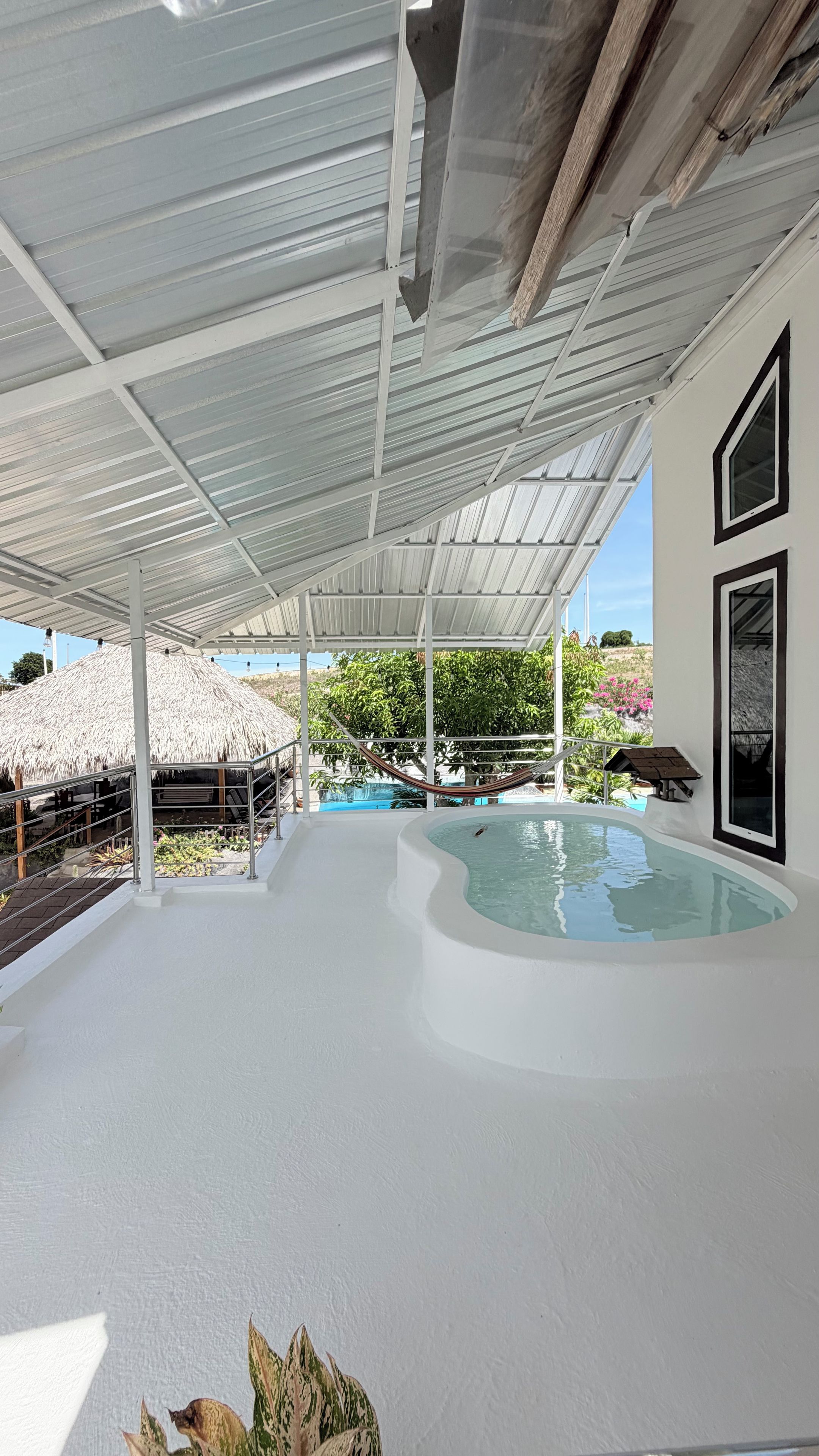 Un espace extérieur abrité avec une piscine, une structure à toit de chaume et un hamac.
