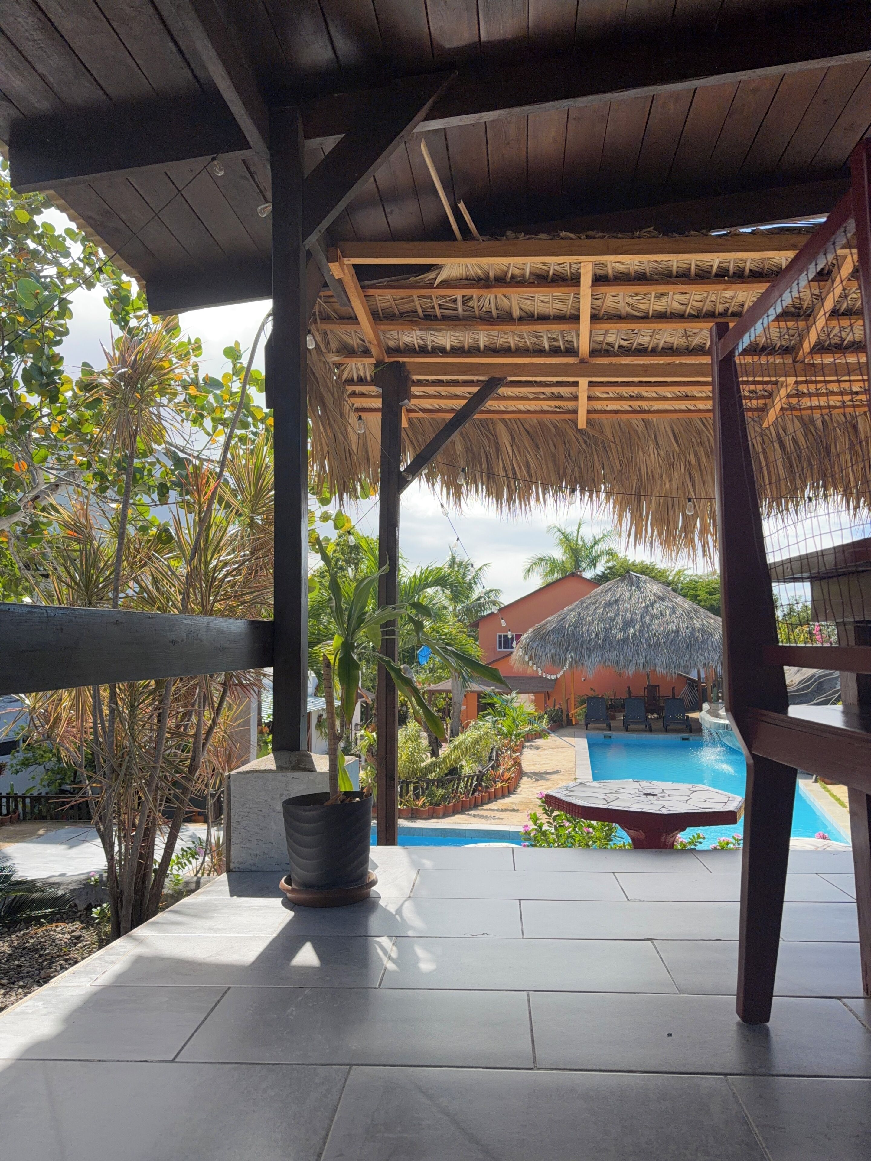 A covered outdoor area with a pool, wooden beams, and potted plants.