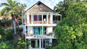 Una casa de dos pisos con balcón, rodeada de vegetación.