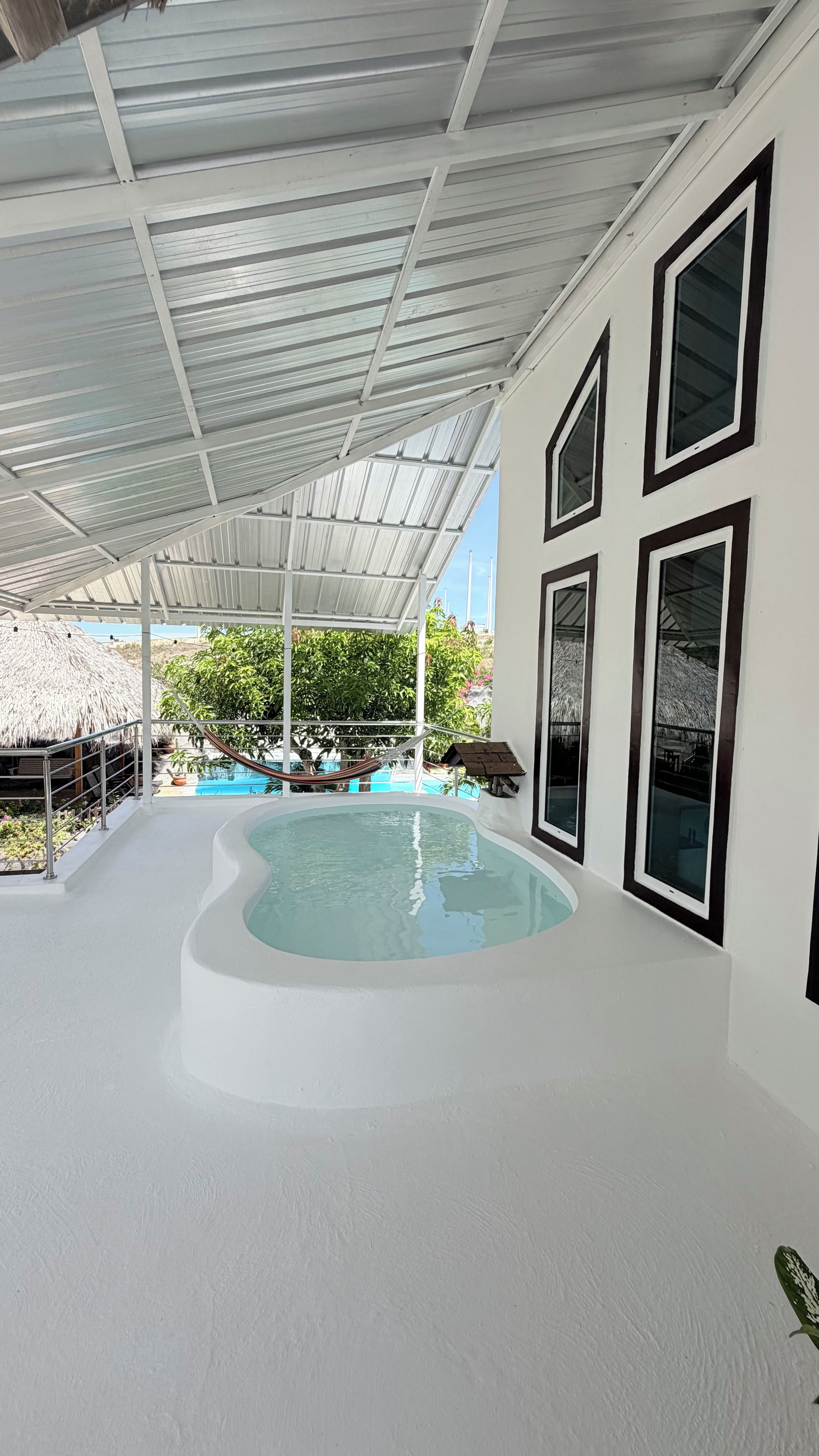 Ein beheiztes Hallenbad mit weißen Innenwänden, umgeben von einem überdachten Bereich mit großen Fenstern und Blick auf Grünflächen.