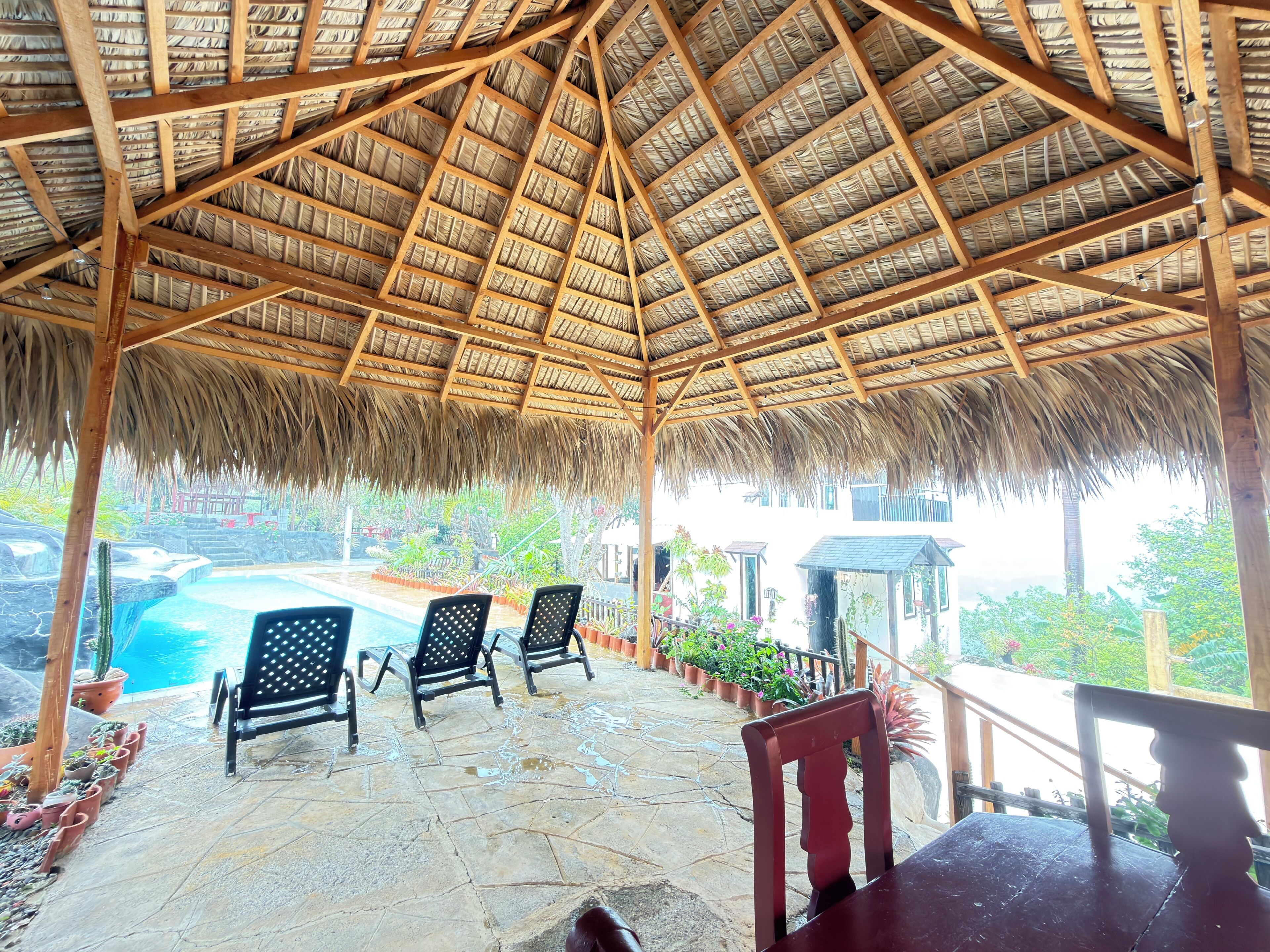 A covered outdoor area with a pool, chairs, and potted plants.